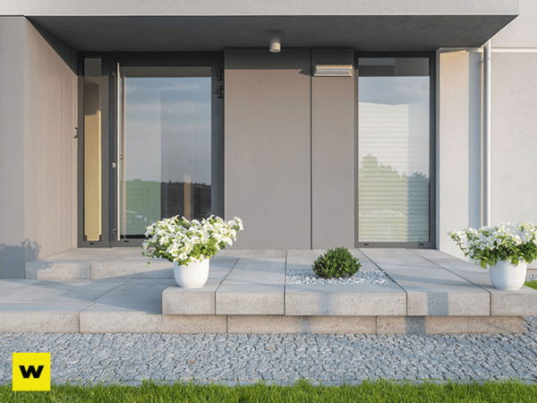 Moderner Hauseingang mit großen Glasflächen, Steinplatten und weißen Blumentöpfen.