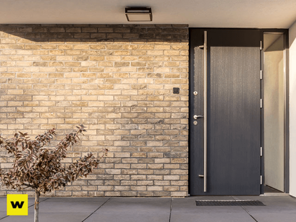 Moderne Hauseingangstür aus dunklem Material in einer Fassade aus hellen Klinkerziegeln.