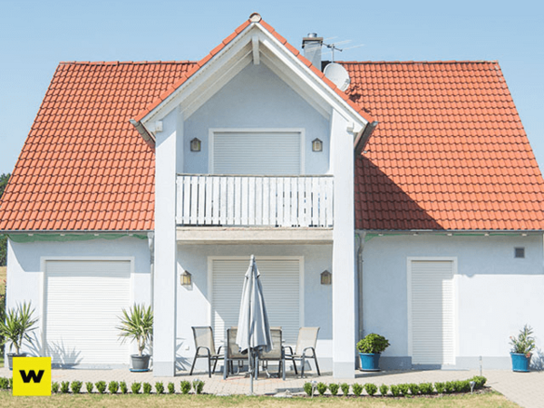 Modernes Einfamilienhaus mit rotem Dach, Balkon und Terrasse im sonnigen Garten.
